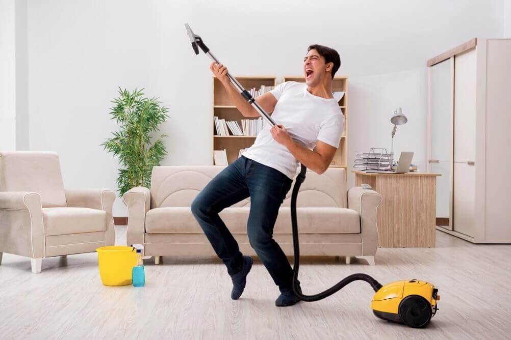 Man dancing with vacuum cleaner in front roon