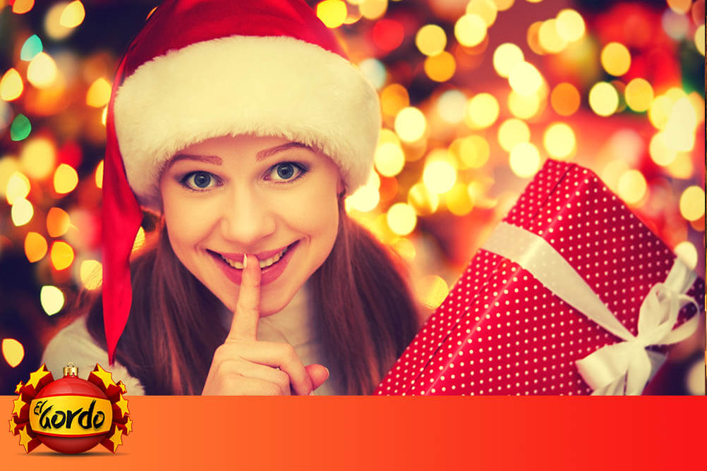 Young woman holding a Christmas gift in front of glittering lights