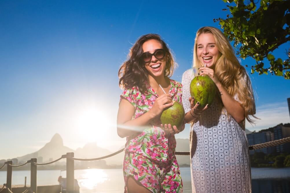 Two women drinking from coconuts on the beach